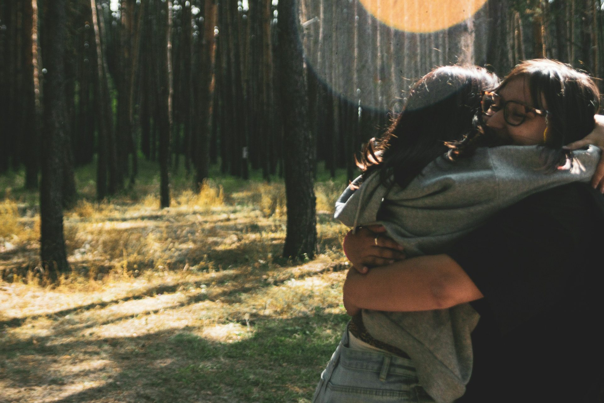 Two people hugging in a sunlit forest.